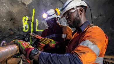 Obuasi Mine workers in protective helmets and orange workwear carry out underground core sample drilling