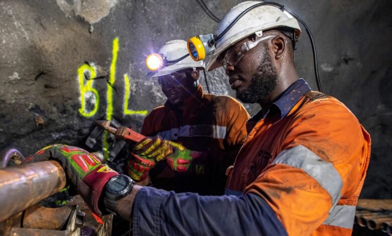 Obuasi Mine workers in protective helmets and orange workwear carry out underground core sample drilling