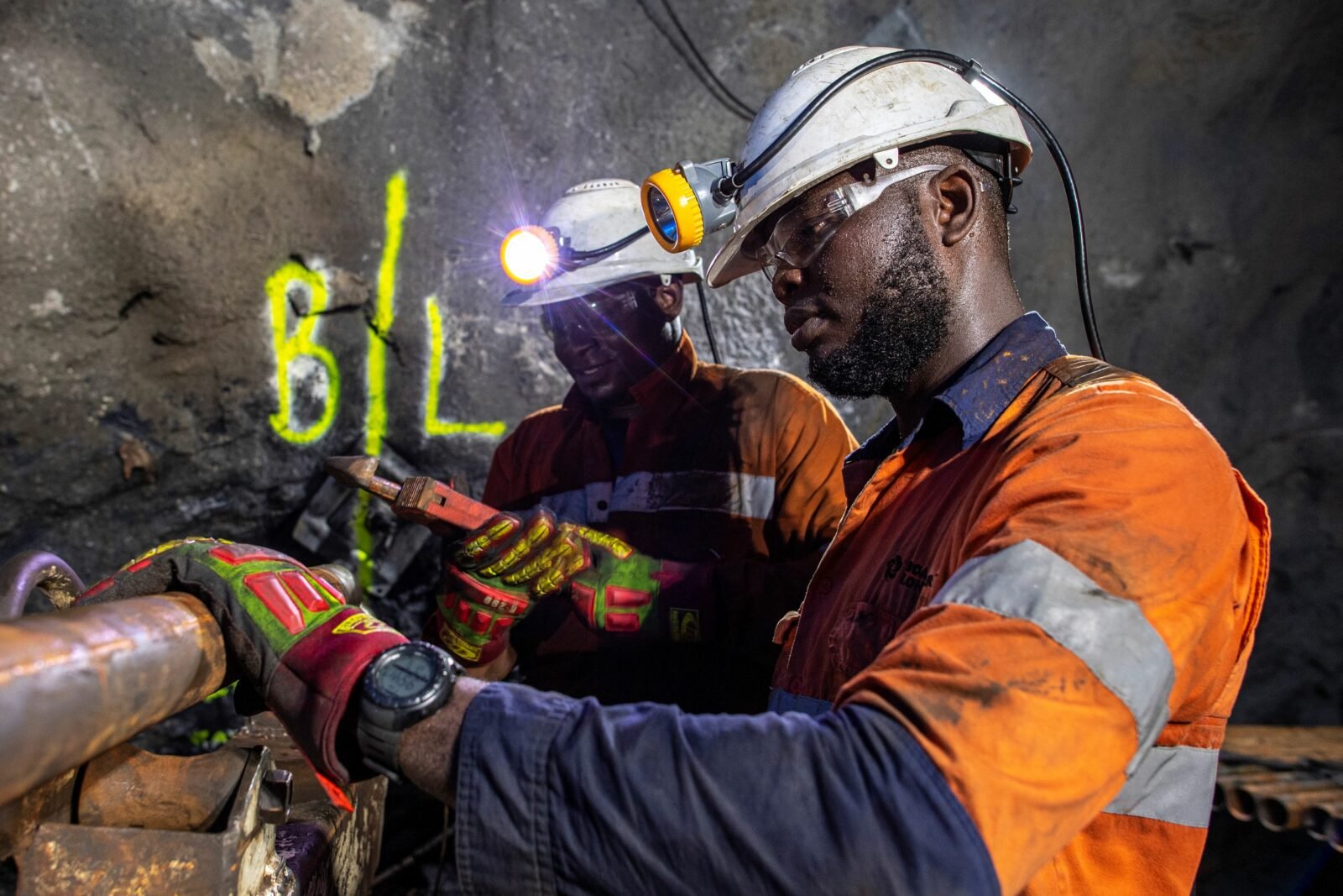 Obuasi Mine workers in protective helmets and orange workwear carry out underground core sample drilling